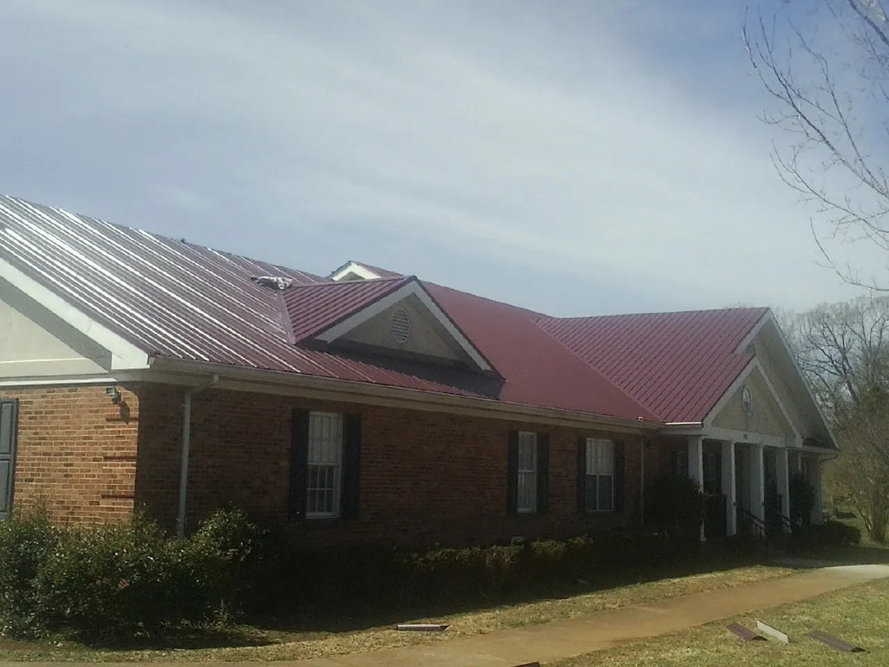 Red metal roof with gabled entries on a long brick building, from a Hail Damage Roof Repair job in Dingle
