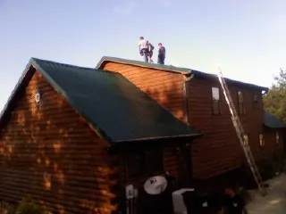 Crew on the ridge of a green metal roof on a two story log home in Dingle