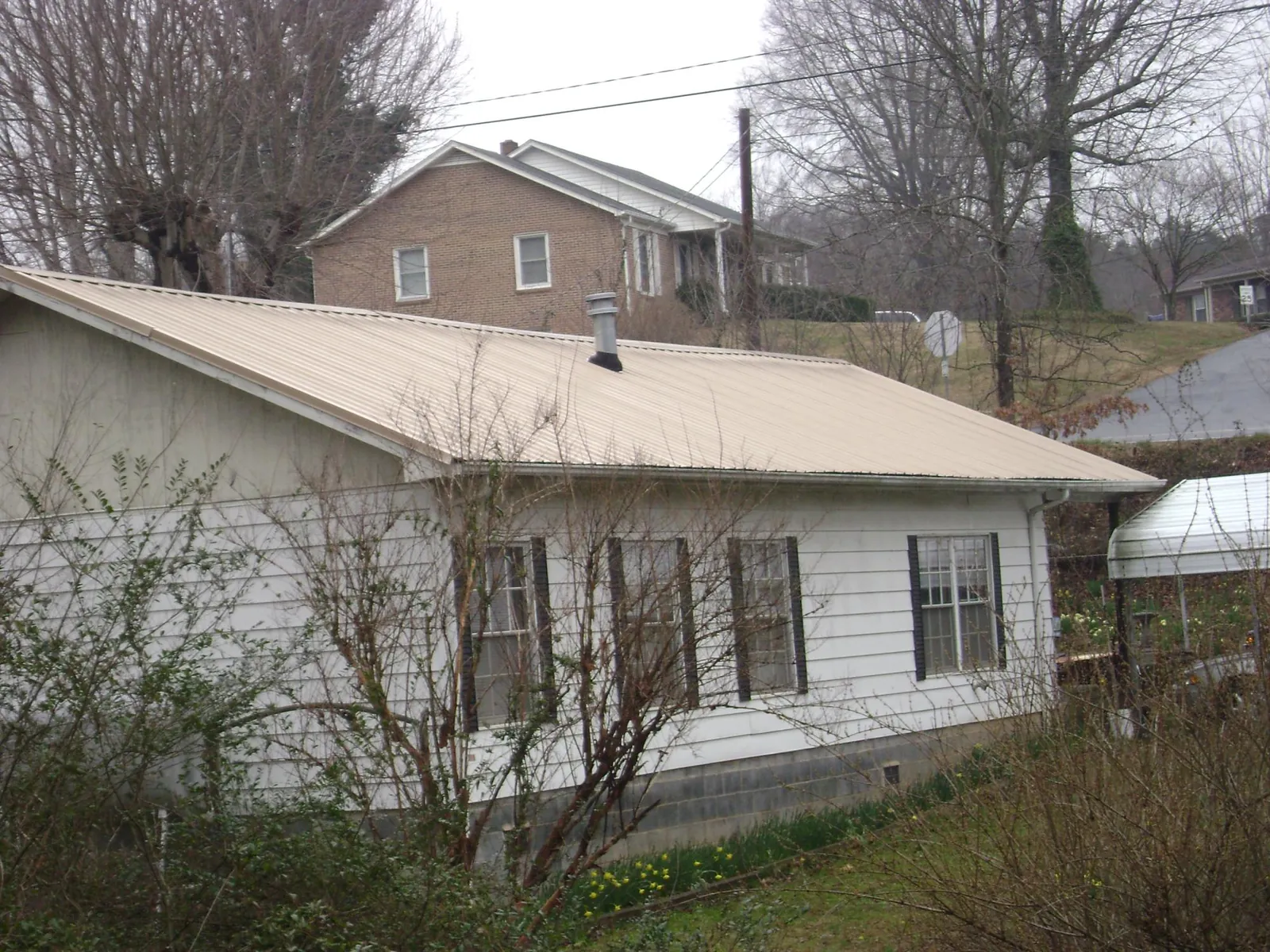 Tan metal roof on a white sided house set into a hillside — Commercial Roofing by Roofing Brothers in Dingle
